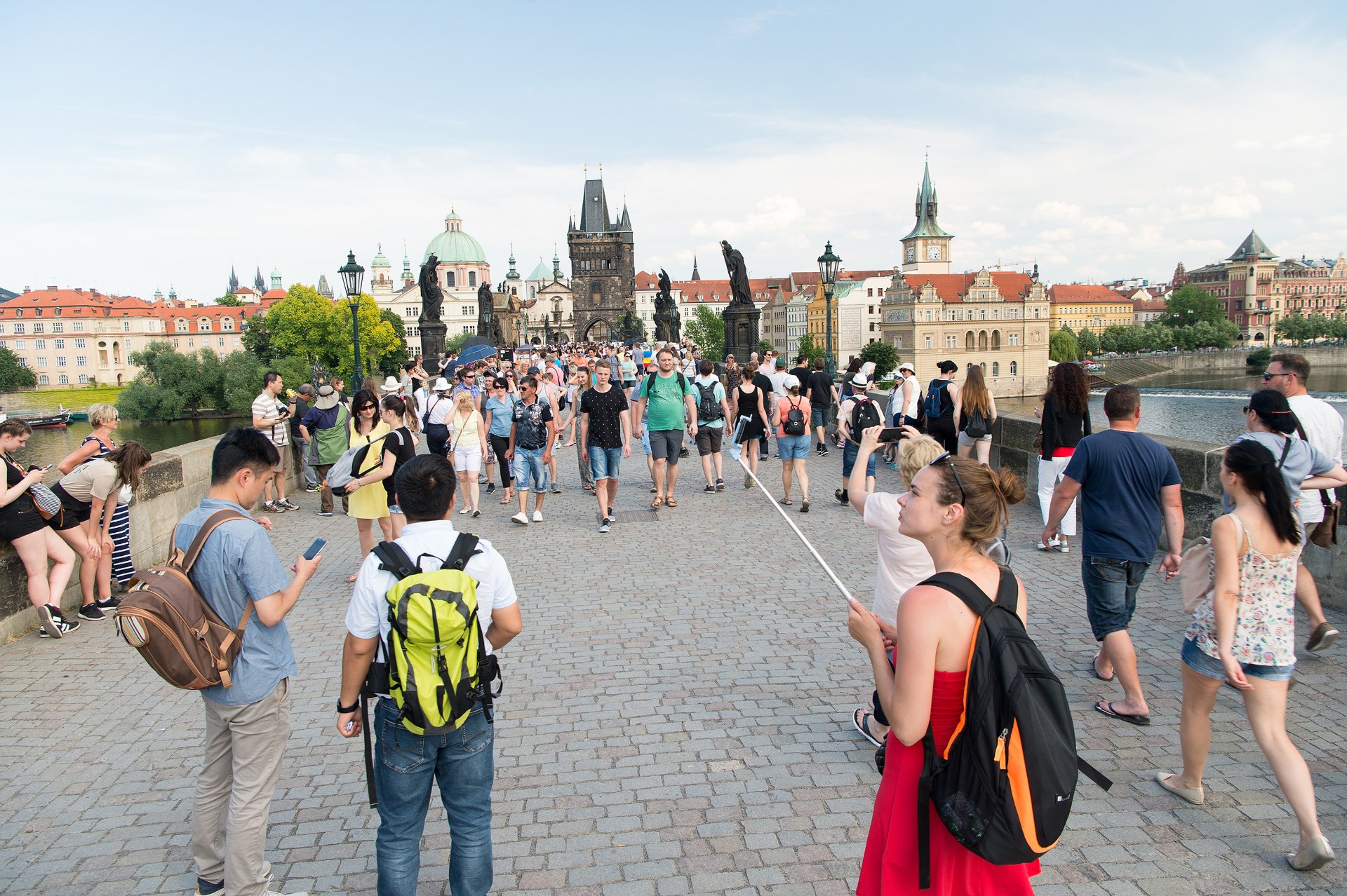 Mladí ľudia s batohmi kráčajú po Karlovom moste v Prahe, v pozadí Staromestská mostná veža